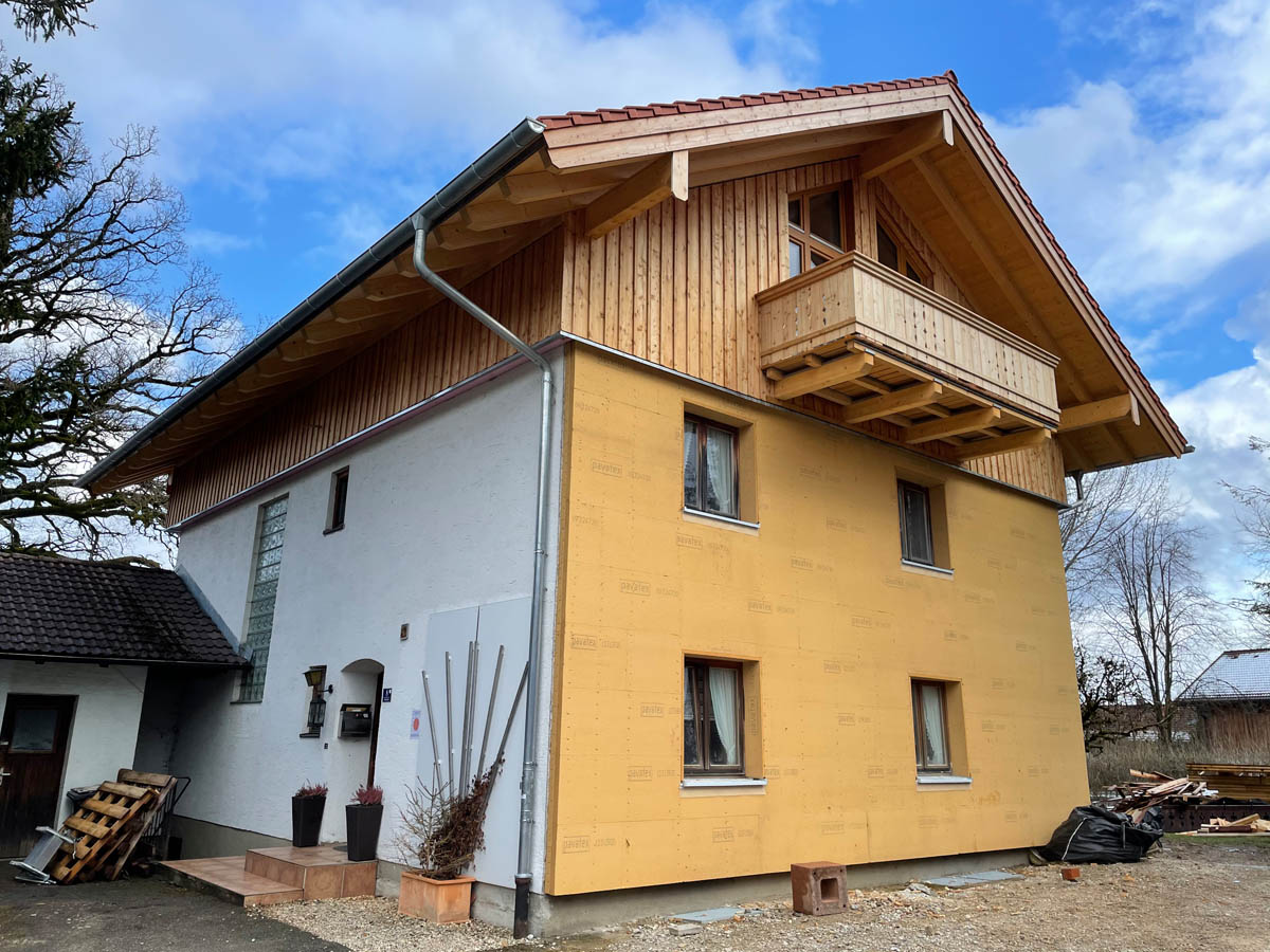Ein zweistöckiges Haus mit einer neuen hölzernen Aufstockung und Balkon unter blauem Himmel.