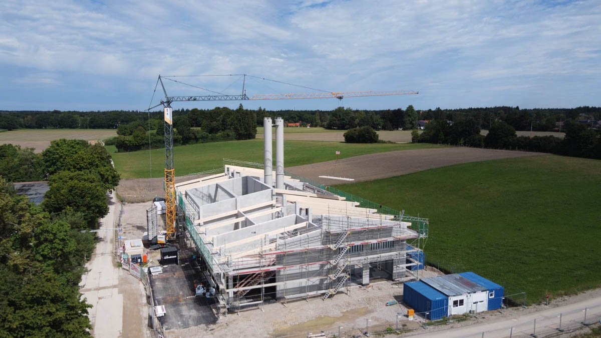 Biomassekraftwerk im Bau auf einem grünen Feld mit Baukran und Containern an der Baustelle.