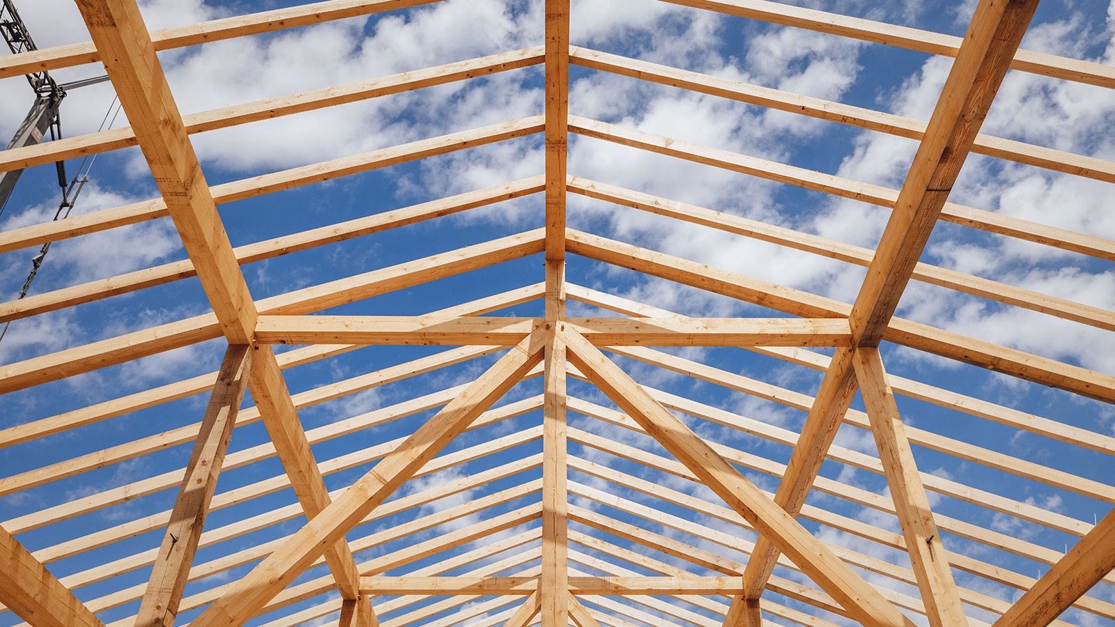 Holzkonstruktion des Hallendachs vor blauem Himmel mit Wolken.