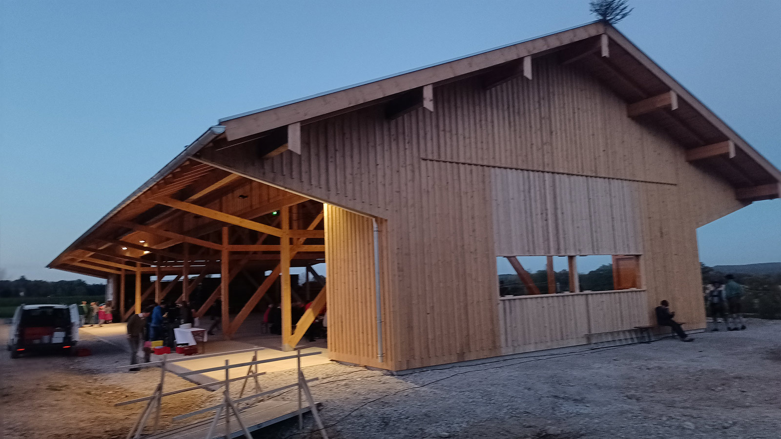 Halle bei Dämmerung, Innenbeleuchtung sichtbar, Menschen davor.