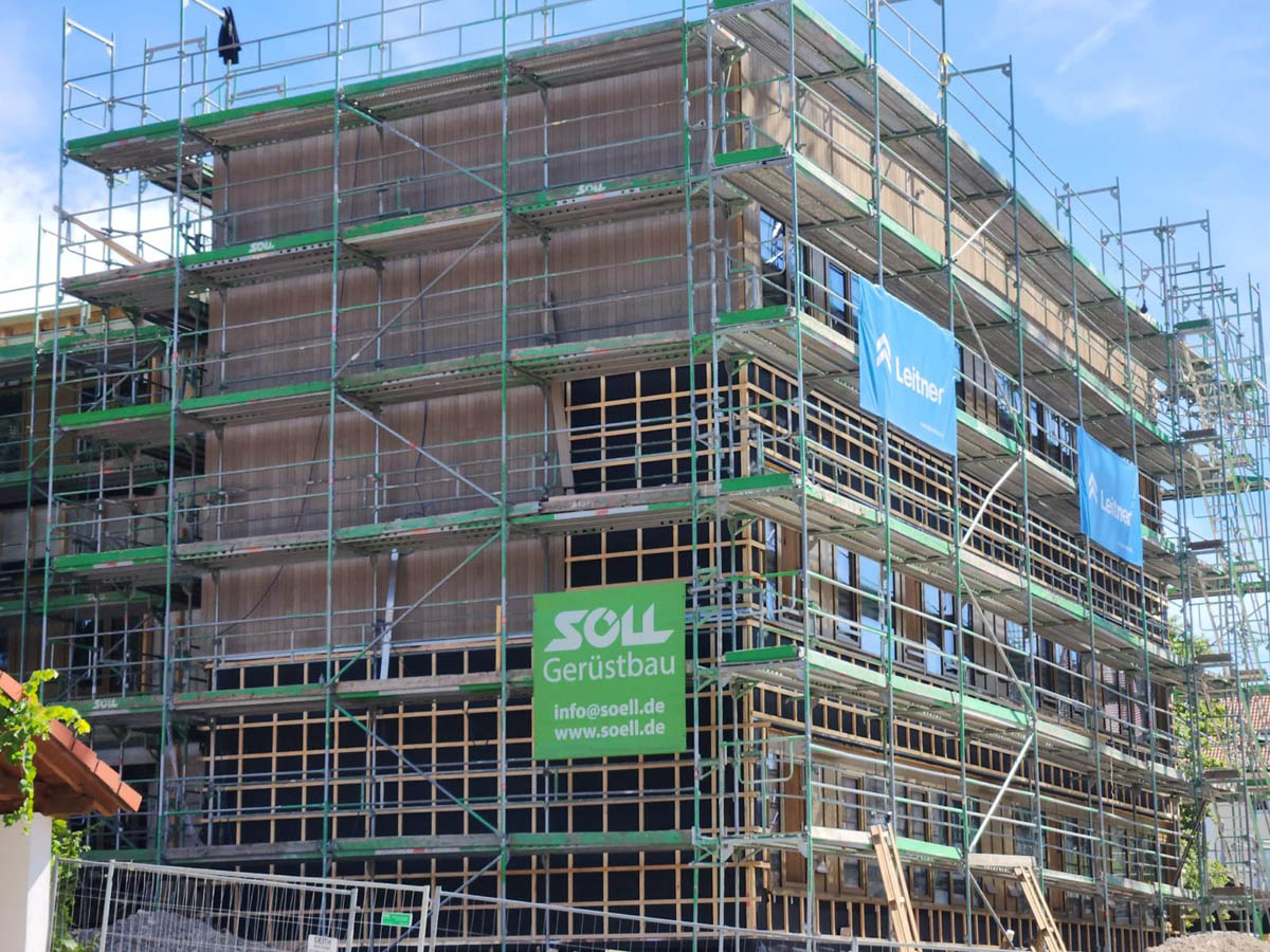 Mehrstöckiges Gebäude unter Bau mit grünem Gerüst und Werbebannern an der Fassade.