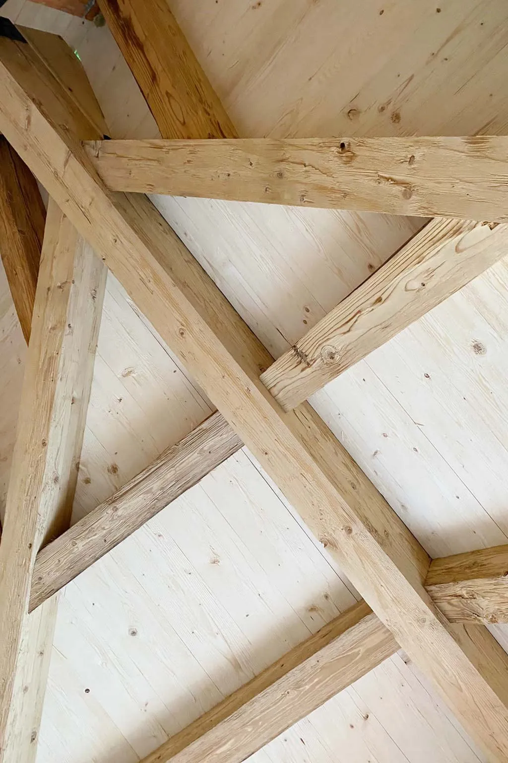Nahaufnahme eines Holzdachstuhls mit sichtbaren Holzbalken und Paneelen.