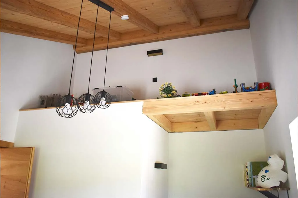 Innenansicht eines Raumes mit einer Holzbalkendecke, drei modernen, schwarzen Hängeleuchten in Käfigdesign und einer hohen Ablagefläche