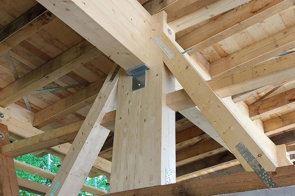 Detailaufnahme der hölzernen Dachkonstruktion einer Scheune, die verschiedene Balken, Streben und Metallverbindungen zeigt.