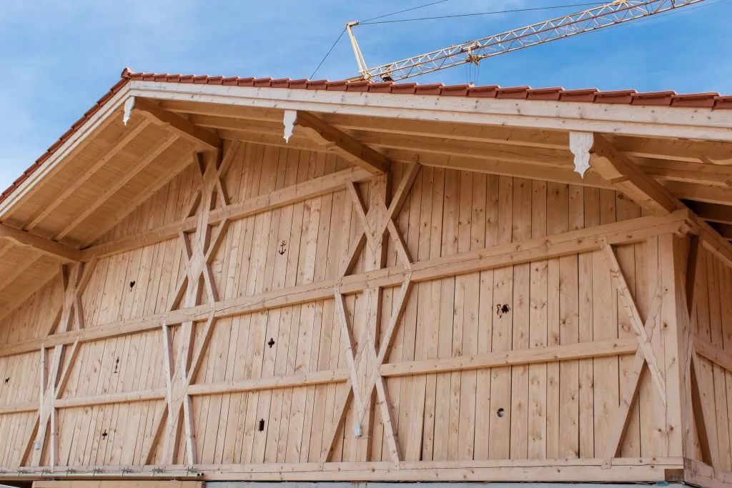 Außenansicht einer Holzkonstruktion mit roten Dachziegeln, geschnitzten Verzierungen und einem Kran im Hintergrund bei blauem Himmel.