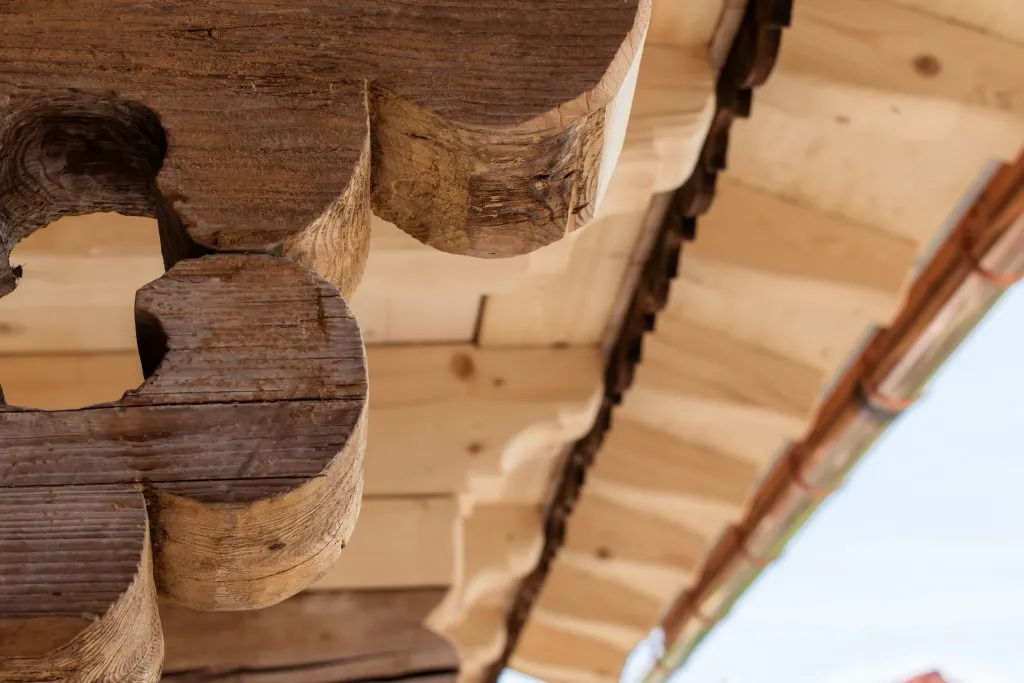 Nahaufnahme einer kunstvoll geschnitzten Holzstrebe eines traditionellen Daches mit Holzschindeln und Kupferdachrinne.